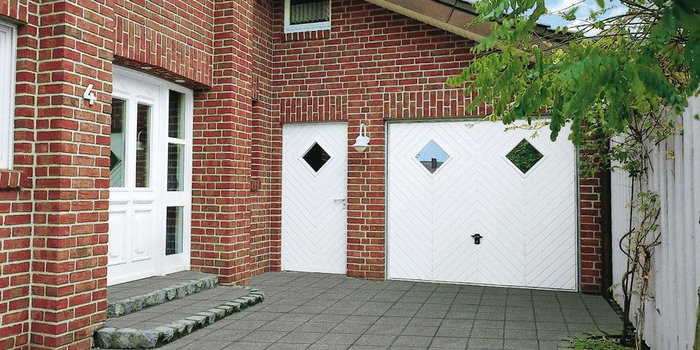 Klinkerhaus mit weißer Tür und weißer Garage mit kleinen Fenstern in nordischem Stil.
